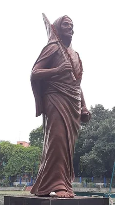 A tall terracotta-coloured statue of Matangini Hazra striding forward with a flagstaff over her shoulder, garlanded with marigolds.